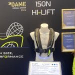 Hermione Barfield from TeamO stands in a booth displaying award winning Hi-Lift Lifejacket. She wears yellow with a black gilet