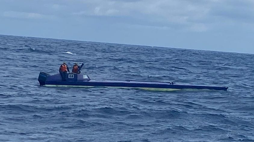 Low, slim narco sub caught smuggling drugs bobs around in ocean pictured with two people in orange lifejackets