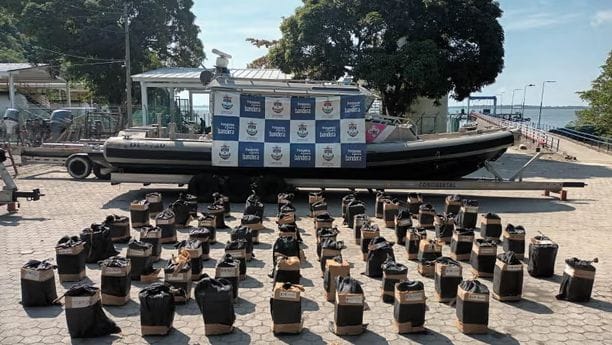 Bags of drugs intercepted in Operation Orion are lined up on cement floor in front of a boat covered by a banner