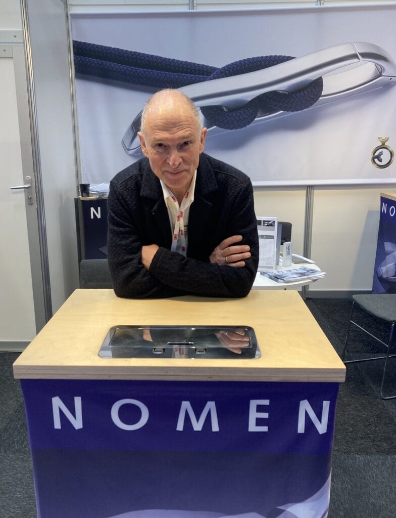 Axel Hoppenhaus from Nomen leans on desk and looks at camera with Nomen branding and pictures of cleat in background