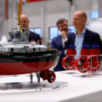 Model of tug on a stand as men stand around and chat