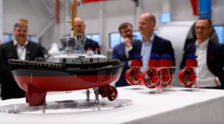 Model of tug on a stand as men stand around and chat