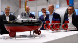 Model of tug on a stand as men stand around and chat