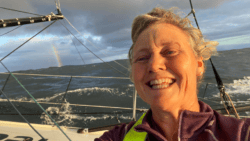 Pip Hare smiles from deck of boat Medallia with a rianbow in the background before dismasting in Vendee Globe a few days later