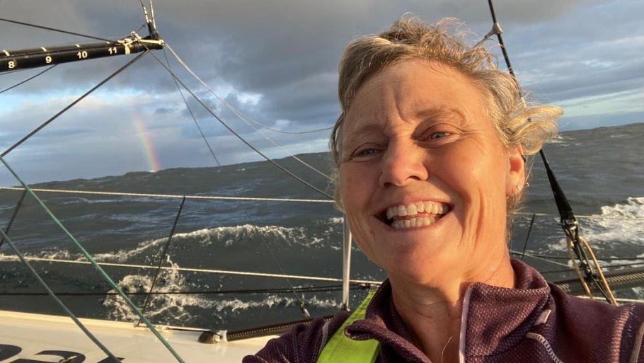 Pip Hare smiles from deck of boat Medallia with a rianbow in the background before dismasting in Vendee Globe a few days later