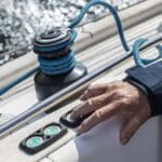 Sailors hand by button winch on sailing boat