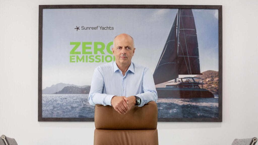 Man leans on back of chair in front of display board with boat showing