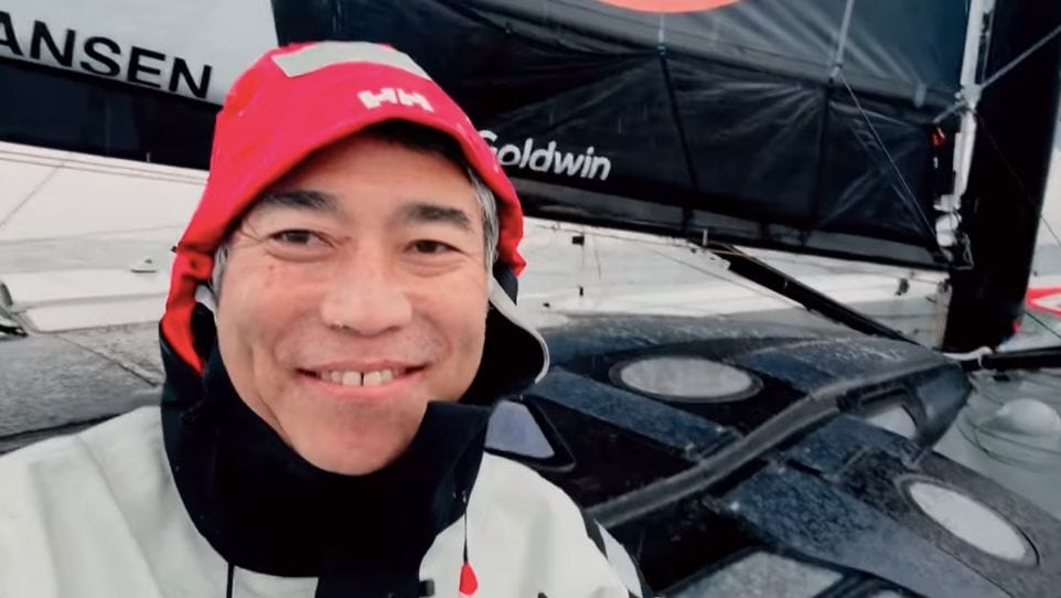 Kojiro Shiraishi smiles at camera from inside his hood onboard boat in Vendee Globe