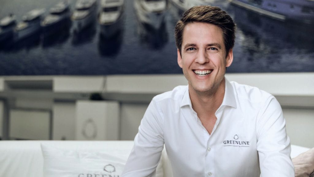 Luca Raumland wears a white shirt and smiles at the camera in front of a display depicting Greenline Yachts' boats