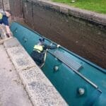 Green canal boat overturned in lock cill as workers try to rescue it from drained lock