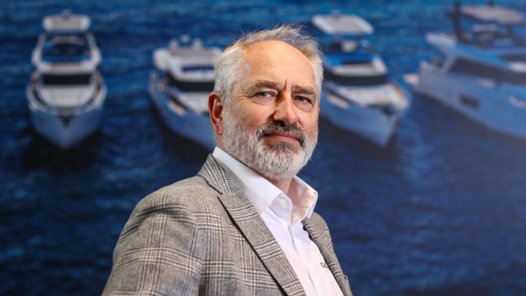 Vladimir Zinchenko wears a grey suit and smiles at the camera in front of a display depicting Greenline Yachts' boats